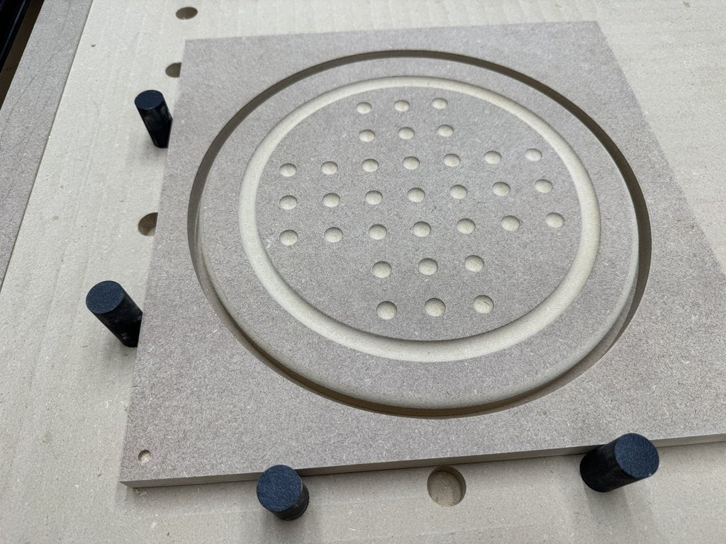 Close-up of a CNC-machined MDF solitaire board prototype with a bottom-left orientation marker